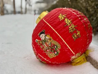 A red Chinese lantern with gold lettering and a colourful figure, resting on snow.